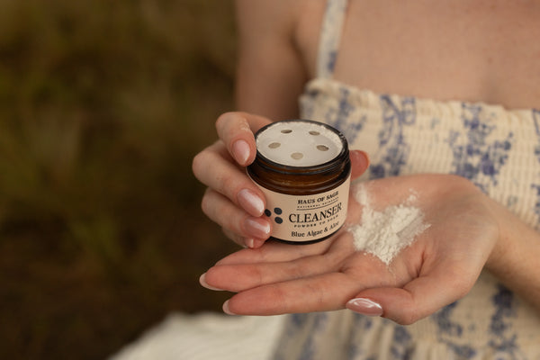 Person holding a jar of facial cleanser with a blurred background
