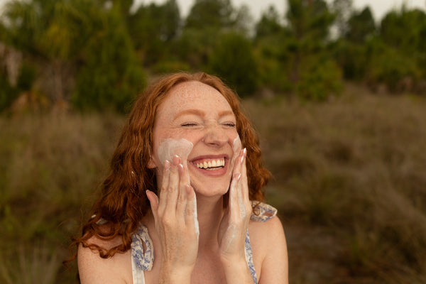 Woman applying cleanser to her face outdoors with a blurred natural background