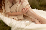 Woman sitting applying creme to her leg next to jar.