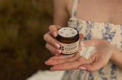Person holding a jar of facial cleanser with a blurred background