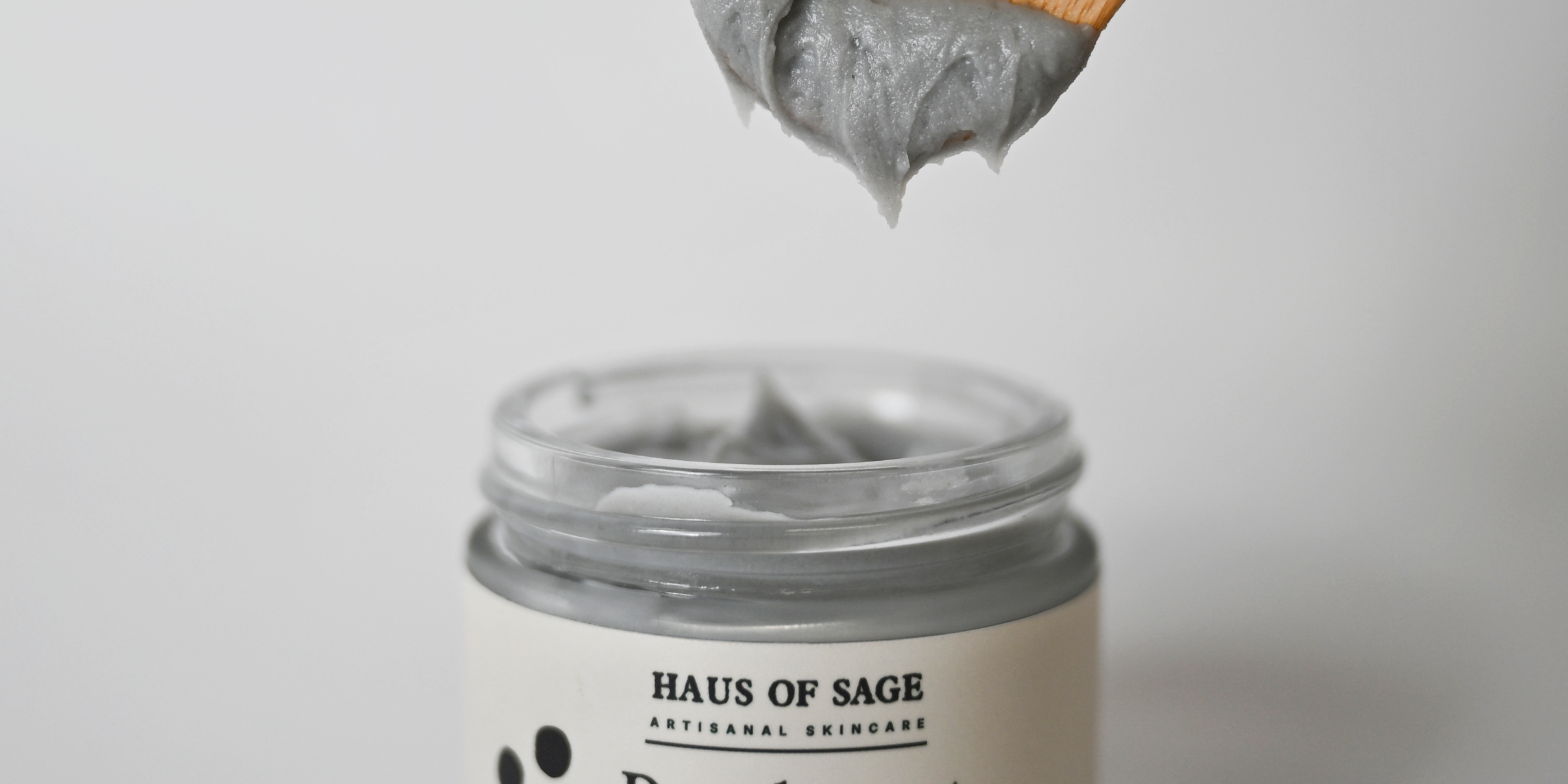 Jar of Haus of Sage deodorant with a wooden applicator on a light gray background