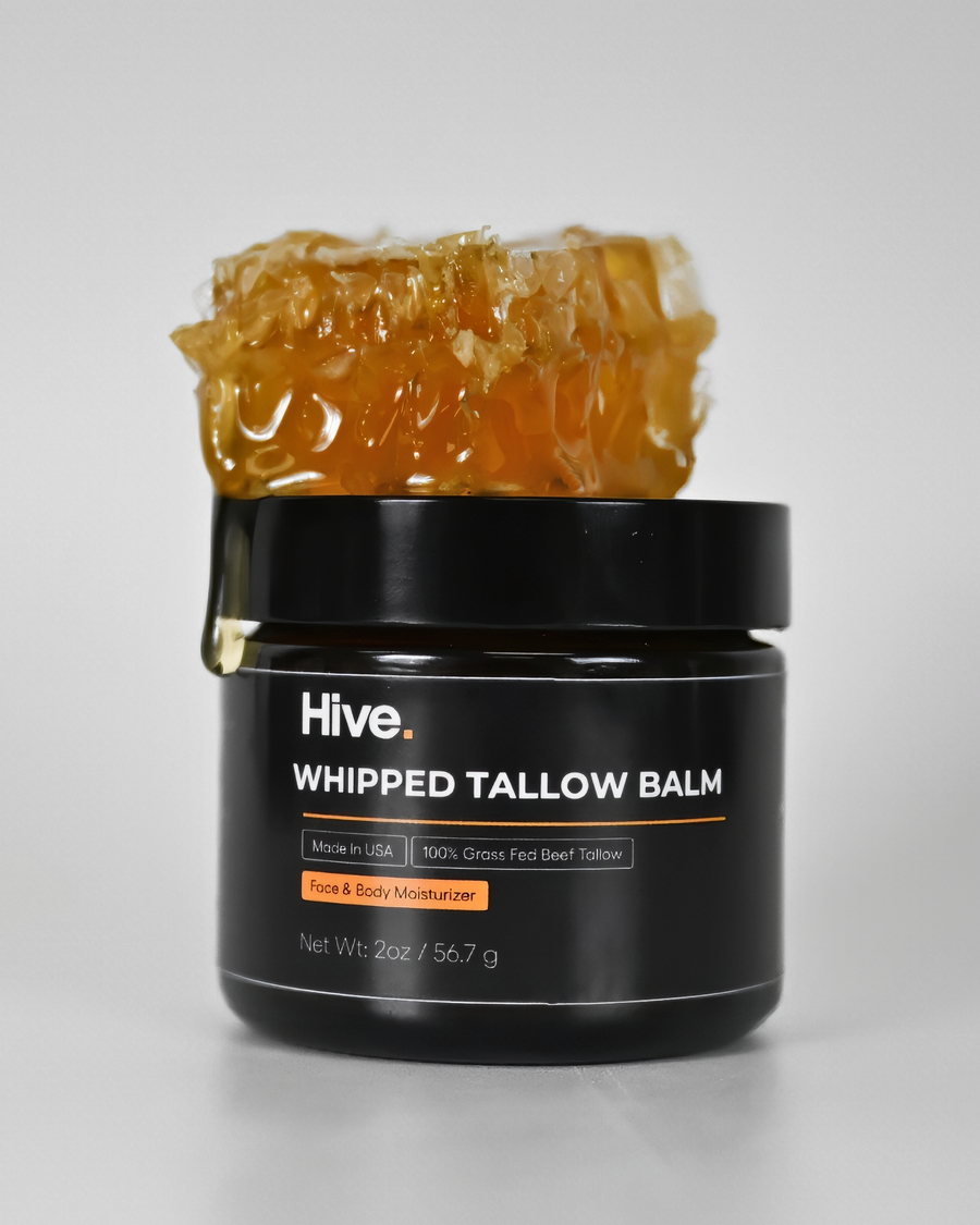 A black jar of Hive Whipped Tallow Balm with a honeycomb piece resting on top, photographed on a clean light gray background.