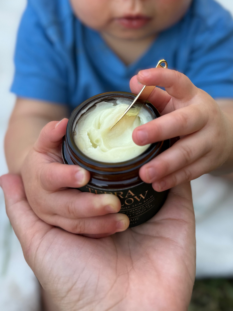 Child holding a jar of cream with a stick, outdoors.