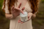 Person holding a jar of 'Haus of Sage Whipped Tallow' balm with a blurred natural background