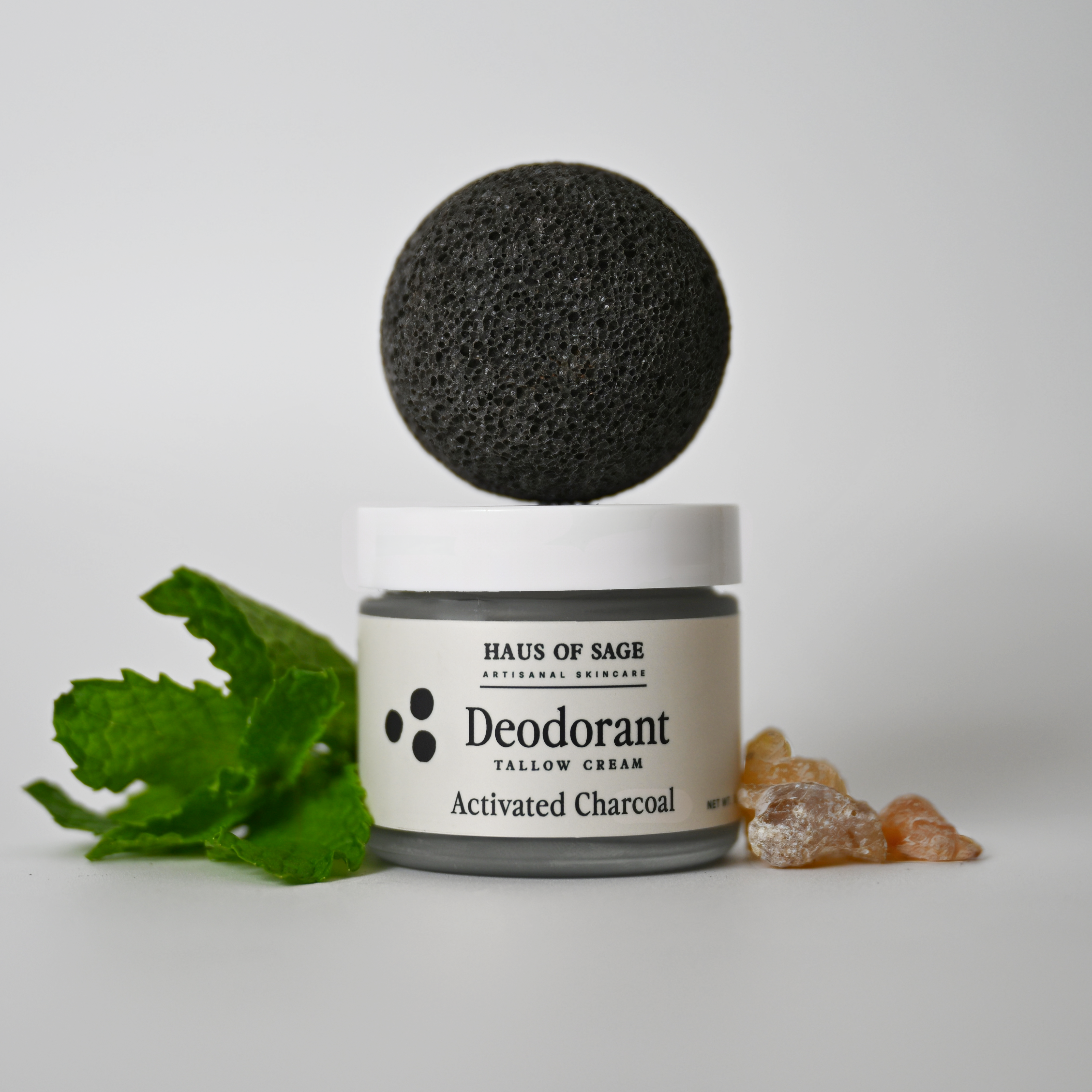Deodorant jar with activated charcoal ball and ginger root on a white background