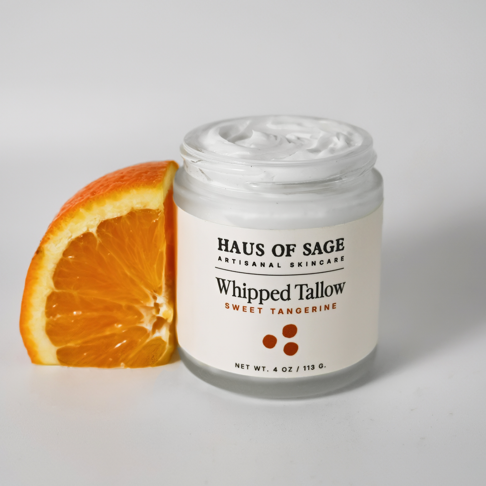 Jar of "Haus of Sage Whipped Tallow Sweet Tangerine" with an orange slice on a white background.